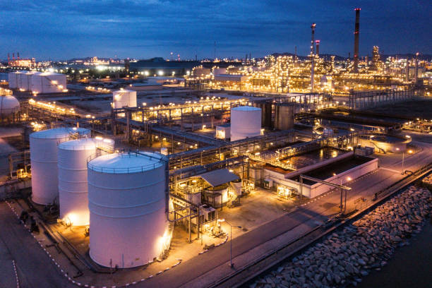 An aerial view of a bustling oil refinery and tank farm, showcasing a complex network of pipelines, storage tanks, and processing facilities. The image captures the industrial scale of the operation, highlighting the importance of petroleum in the global economy. The vibrant blue water surrounding the facility adds a striking contrast to the grey metal structures, creating a compelling visual. This photo is ideal for illustrating the infrastructure of the oil and gas industry, energy production, and industrial landscapes.